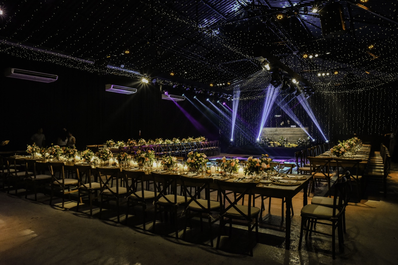 Salón con mesas largas, flores y DJ con luces